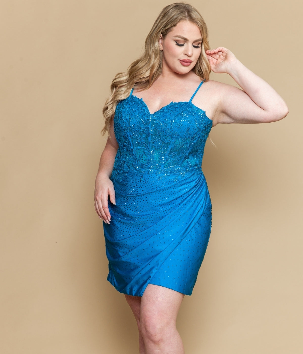 A woman models the Short Plus Size Homecoming Dress: Poly USA W1200— a sleeveless, fitted blue dress with lace appliques on the bodice—standing against a beige background, perfect for homecoming.